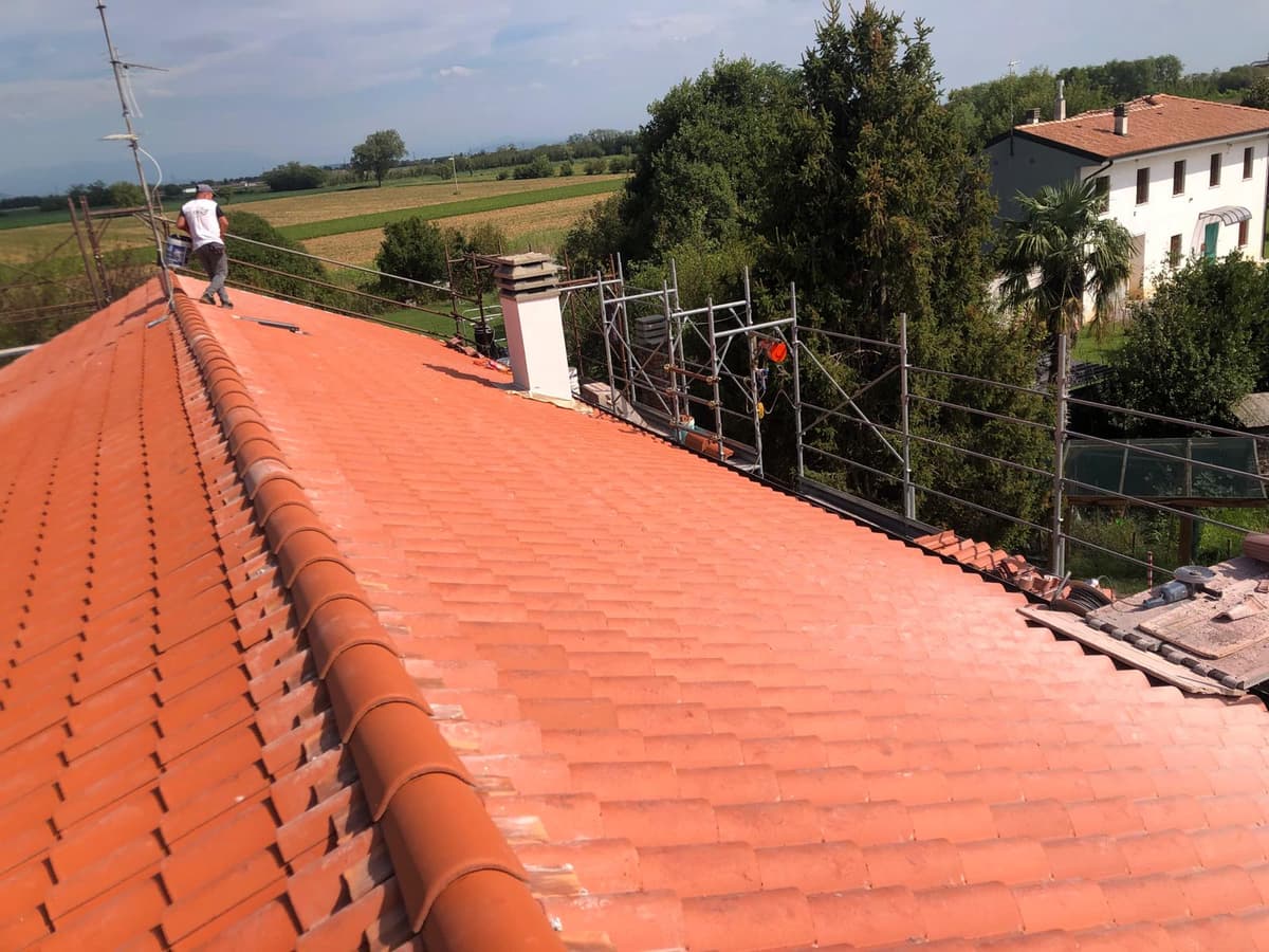 Tetto rifatto con tegole in cotto e operaio al lavoro